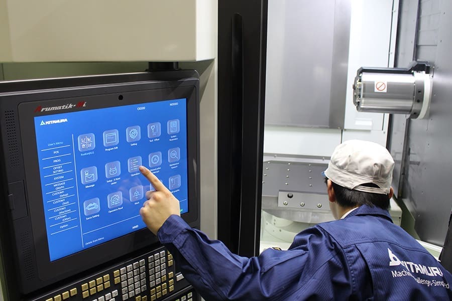 Operator uses touch screen control panel on a Kitamura CNC machine, preparing the horizontal machining center for operation.